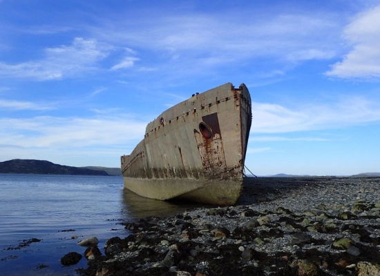 Historic concrete shipwreck at Fevag, Trøndelag - abandoned vessel on rocky shoreline with fjord and mountains in background
