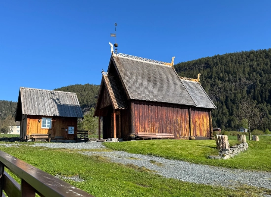 Historic wooden stave church and traditional buildings at Hindrem, Trøndelag, Norway with forested mountains in background