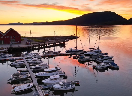 Hasselvika marina at sunset with boats moored in calm fjord waters, red boathouse and mountain silhouettes in Trøndelag, Norway